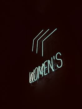 Illuminated neon 'Women's' sign glowing softly in Shibuya, Tokyo at nighttime.