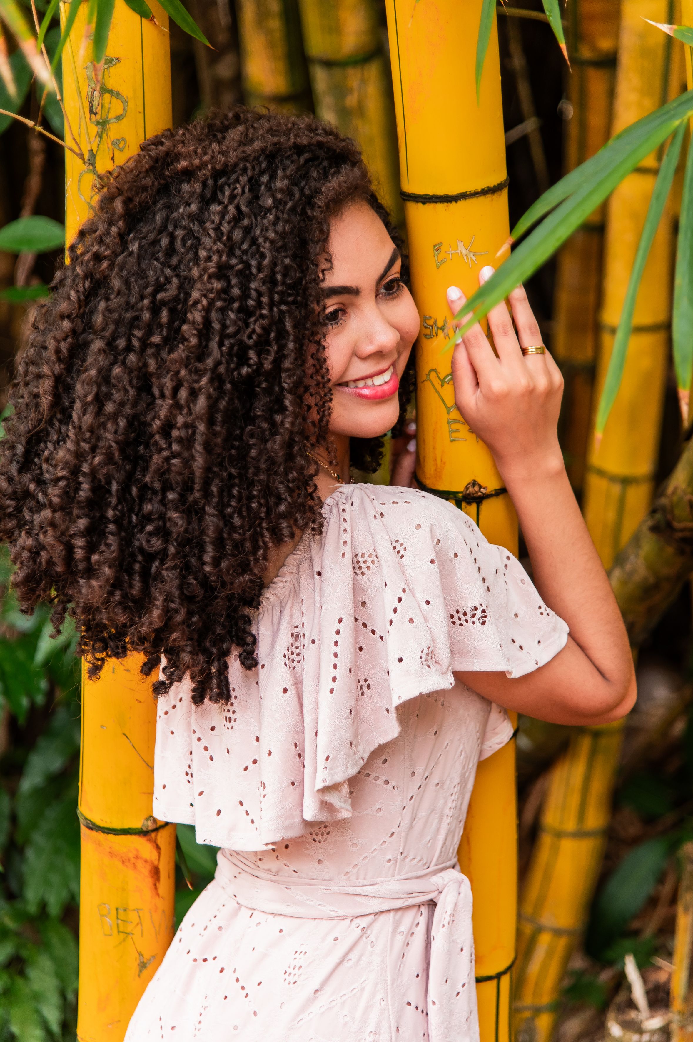 A cheerful woman embraces vibrant yellow bamboo stalks in a lush Bahia setting, radiating happiness and nature's beauty.