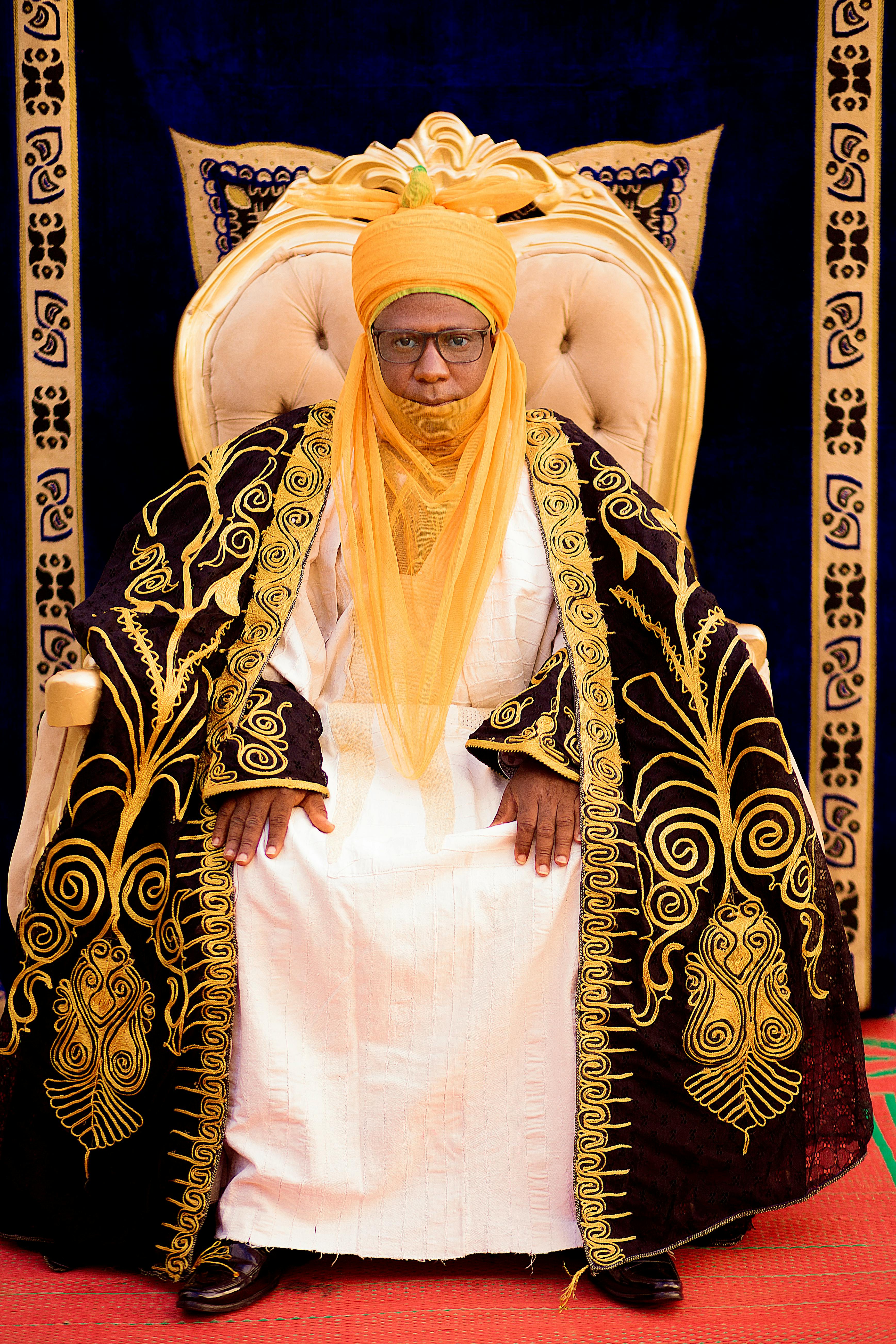 Regal figure in traditional African attire with intricate gold embroidery and royal decor.