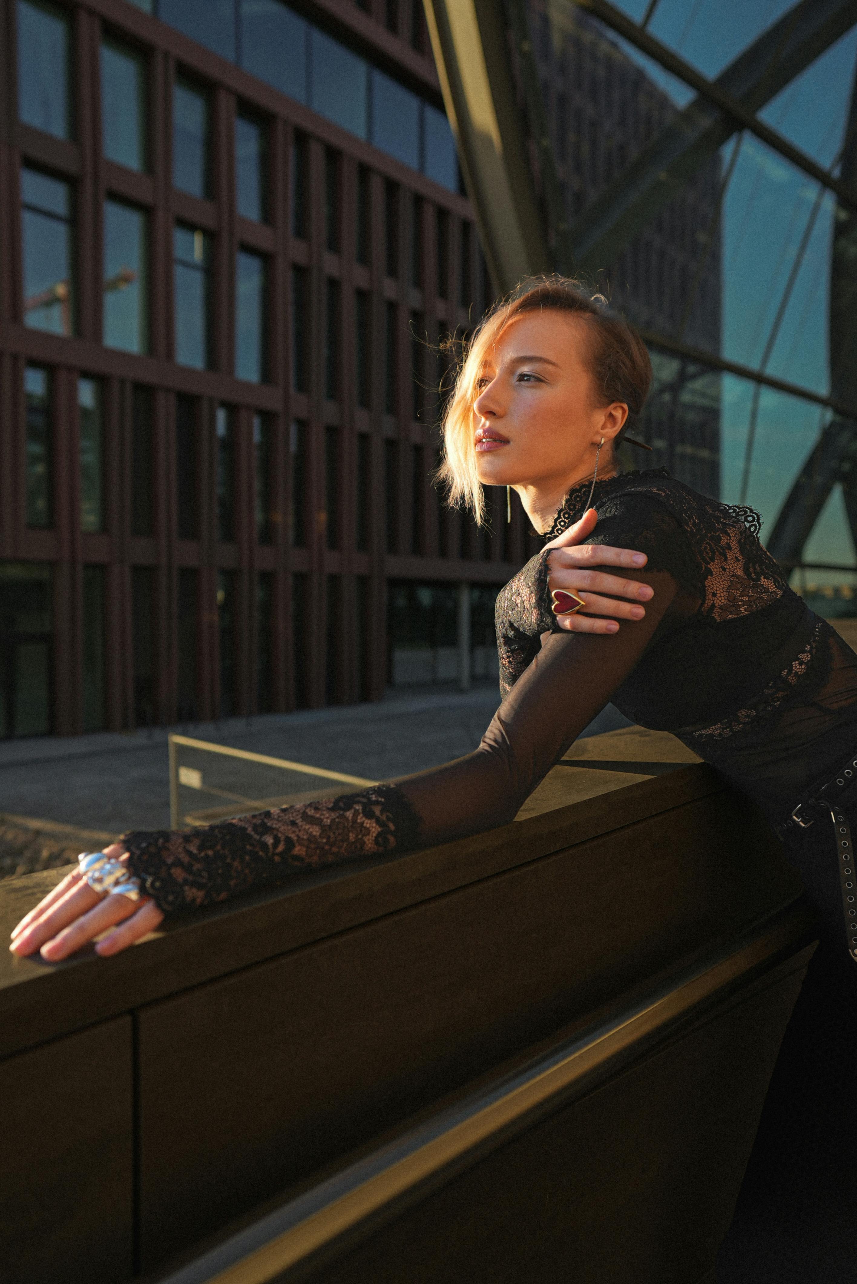 Stylish woman in black lace outfit poses outdoors in Hamburg's cityscape.