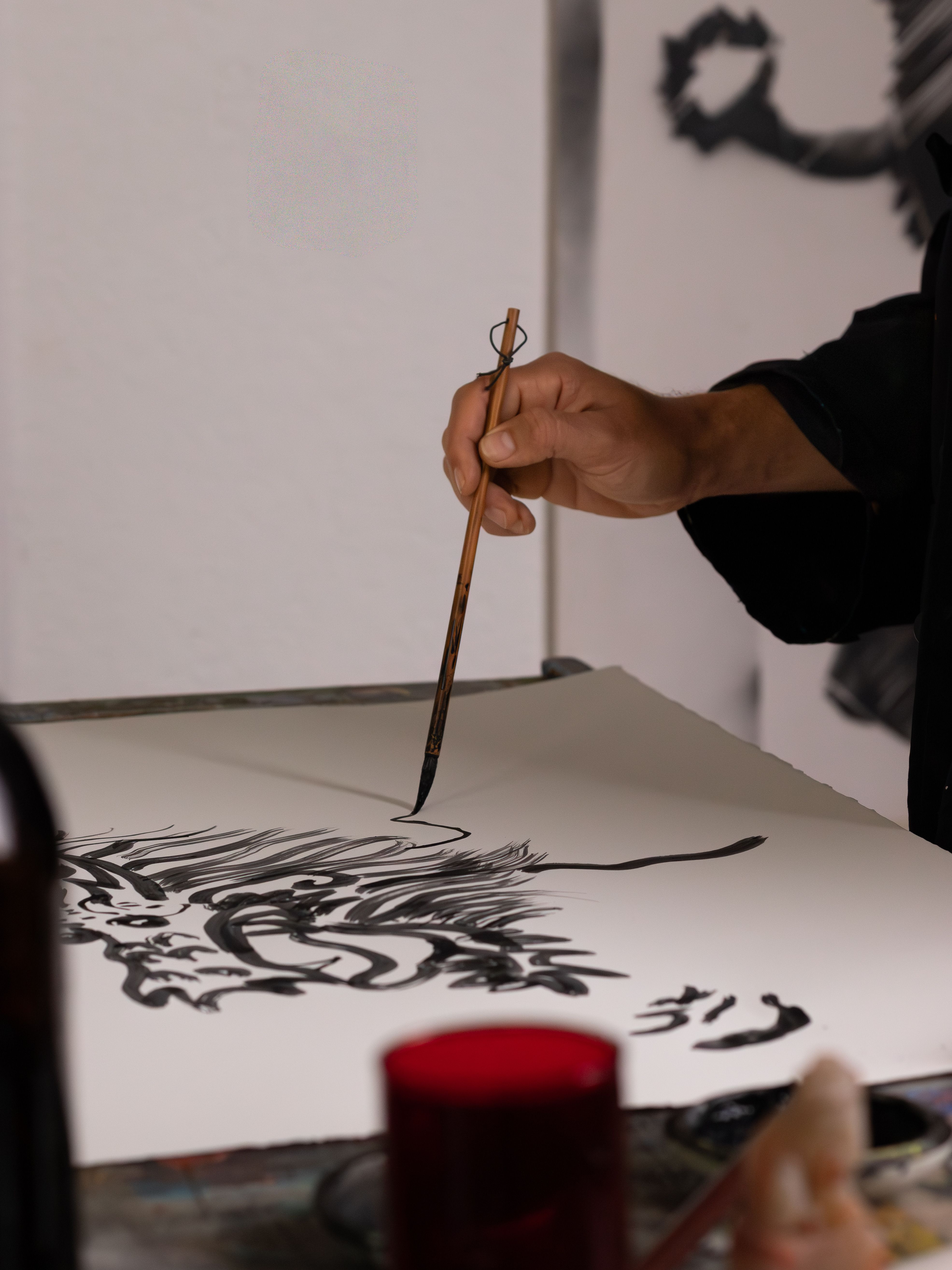 Close-up of an artist creating a black ink painting with a fine brush on paper.