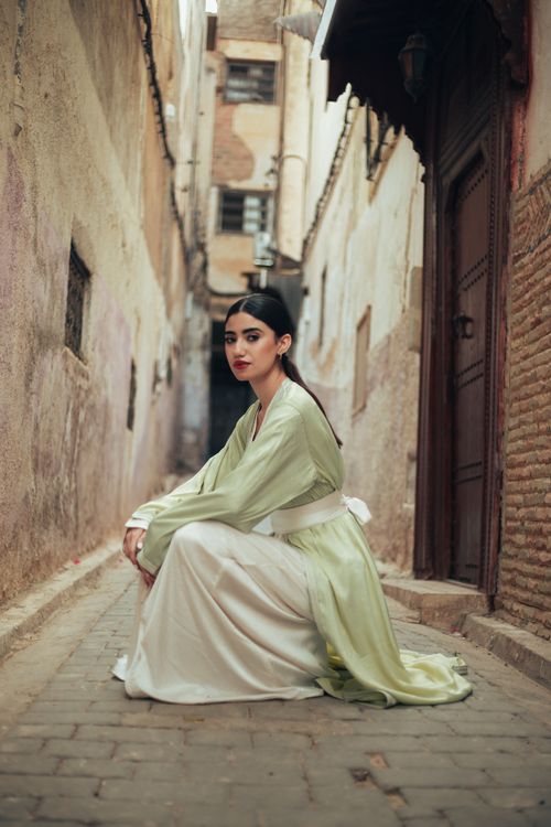 Free Elegant woman in a green dress poses in a narrow historic alleyway with rustic walls. Stock Photo