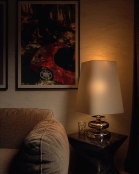 Warm interior scene featuring a modern table lamp, a cozy sofa, and framed car artwork on the wall.