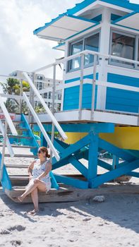 Woman in summer dress relaxing by a colorful lifeguard tower on a sunny beach day.