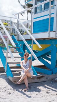 Woman sitting on stairs of a colorful lifeguard tower enjoying a sunny beach day.