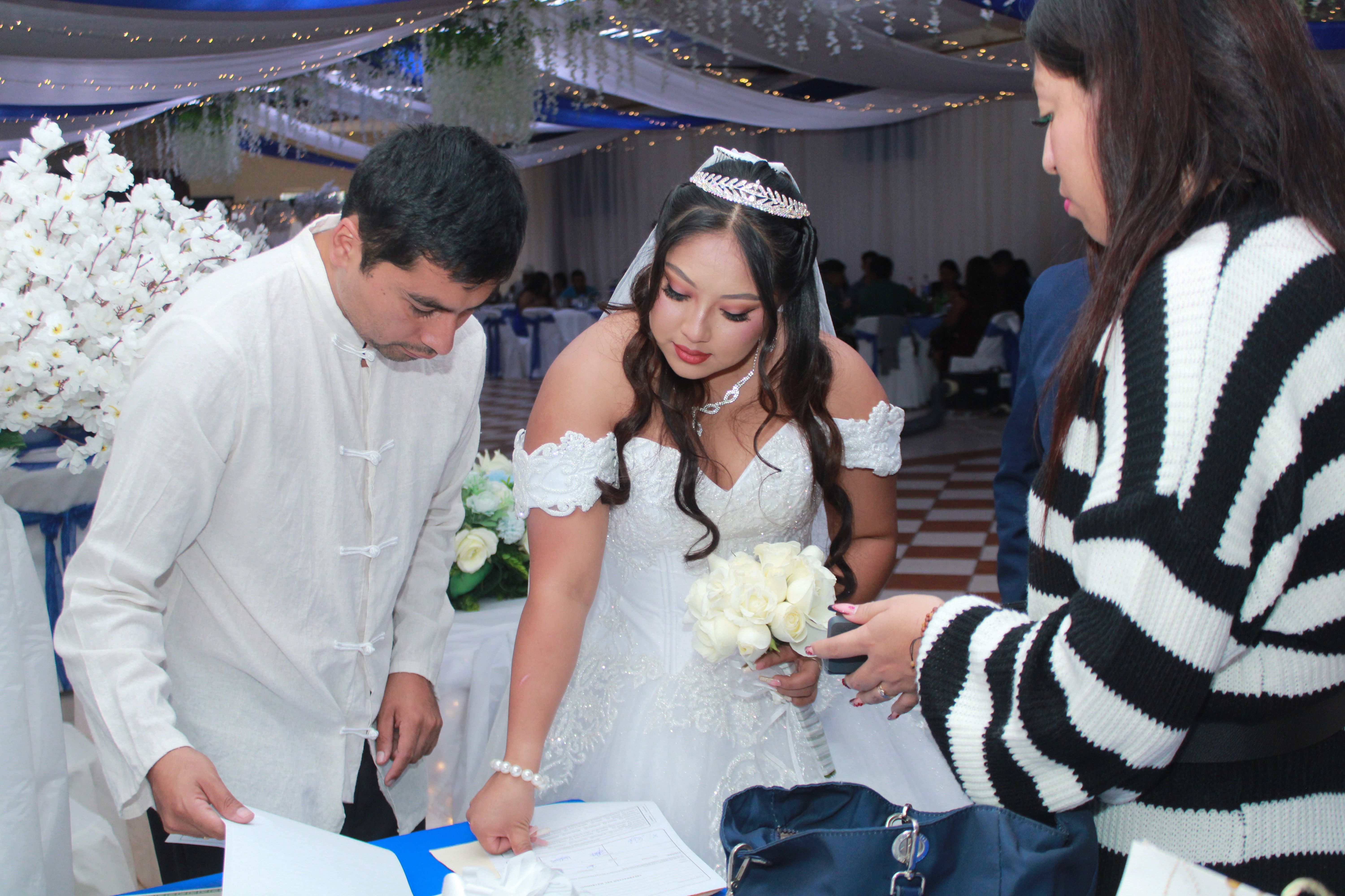 Bride signs a document at an elegant wedding ceremony surrounded by guests.