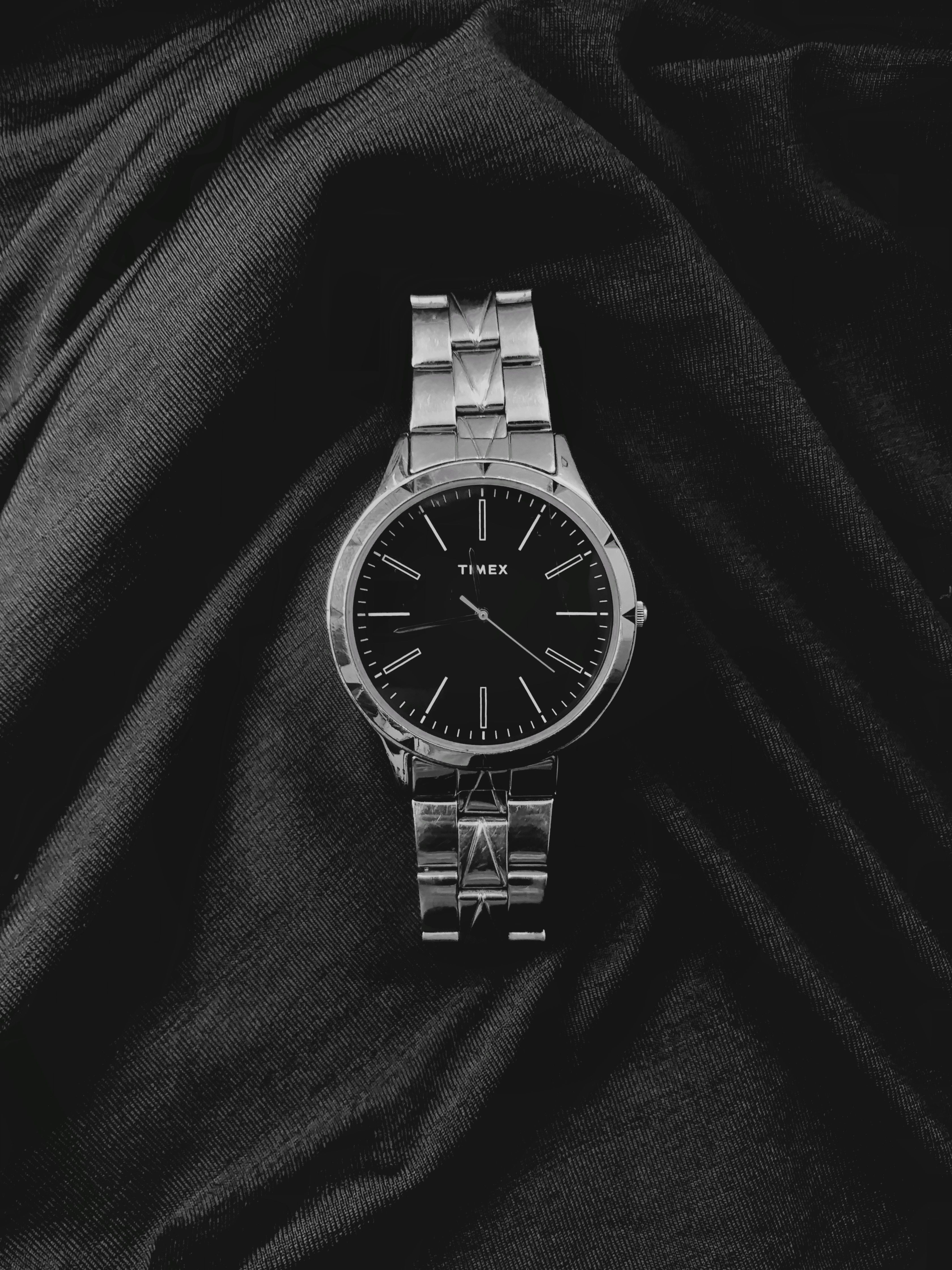 Elegant black and silver Timex watch, creatively showcased on dark fabric for a classic look.