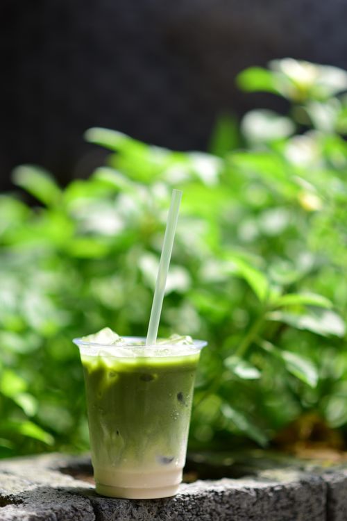 Free Iced matcha latte in a plastic cup placed on stone with a blurred green background outdoors. Stock Photo
