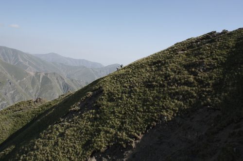 Free Hikers traverse a lush grassy ridge on a clear mountain day, showcasing natural beauty. Stock Photo