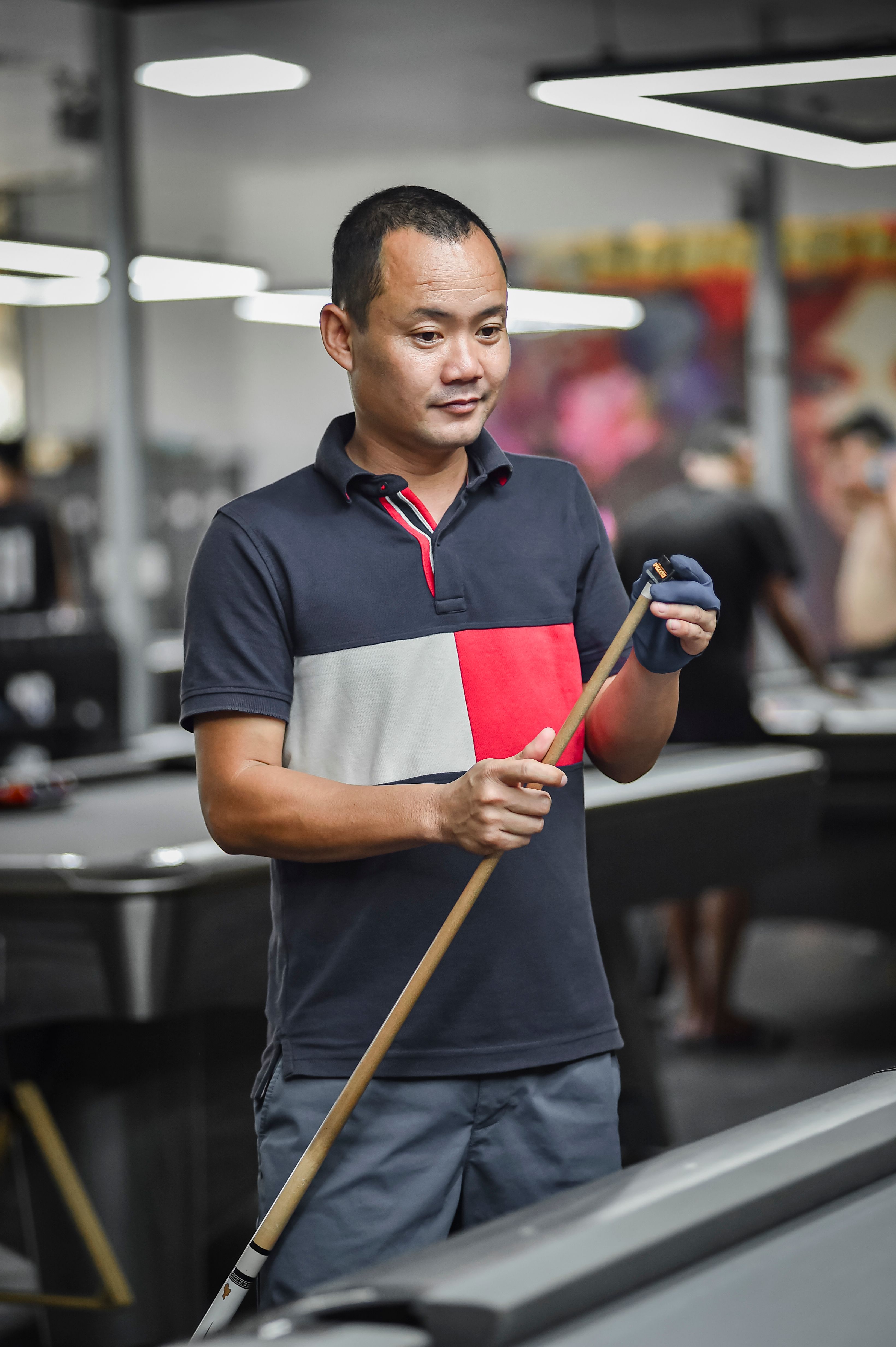 Man holding a pool cue in a modern indoor pool hall in Hanoi, Vietnam.