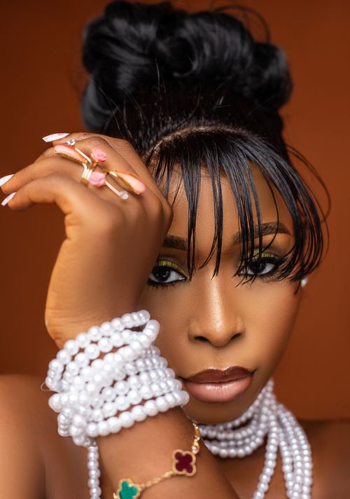 Free Close-up portrait of a woman adorned with elegant pearl jewelry and intricate rings against a warm backdrop. Stock Photo