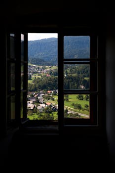 A picturesque valley landscape seen through an open wooden window frame.