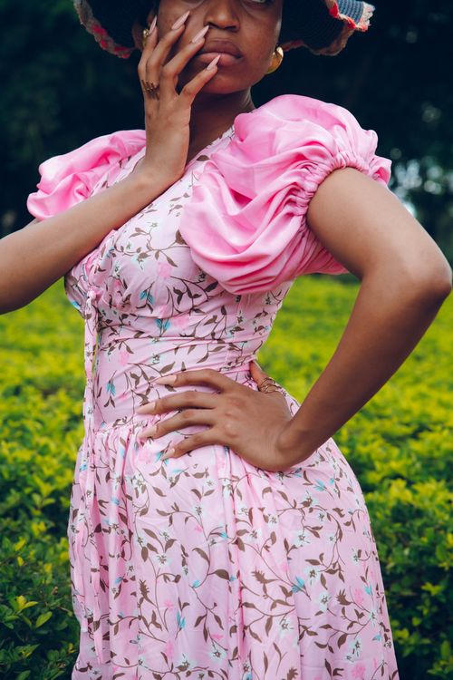 Free Fashion-forward woman in a floral pink dress posing outdoors in a lush green park. Stock Photo