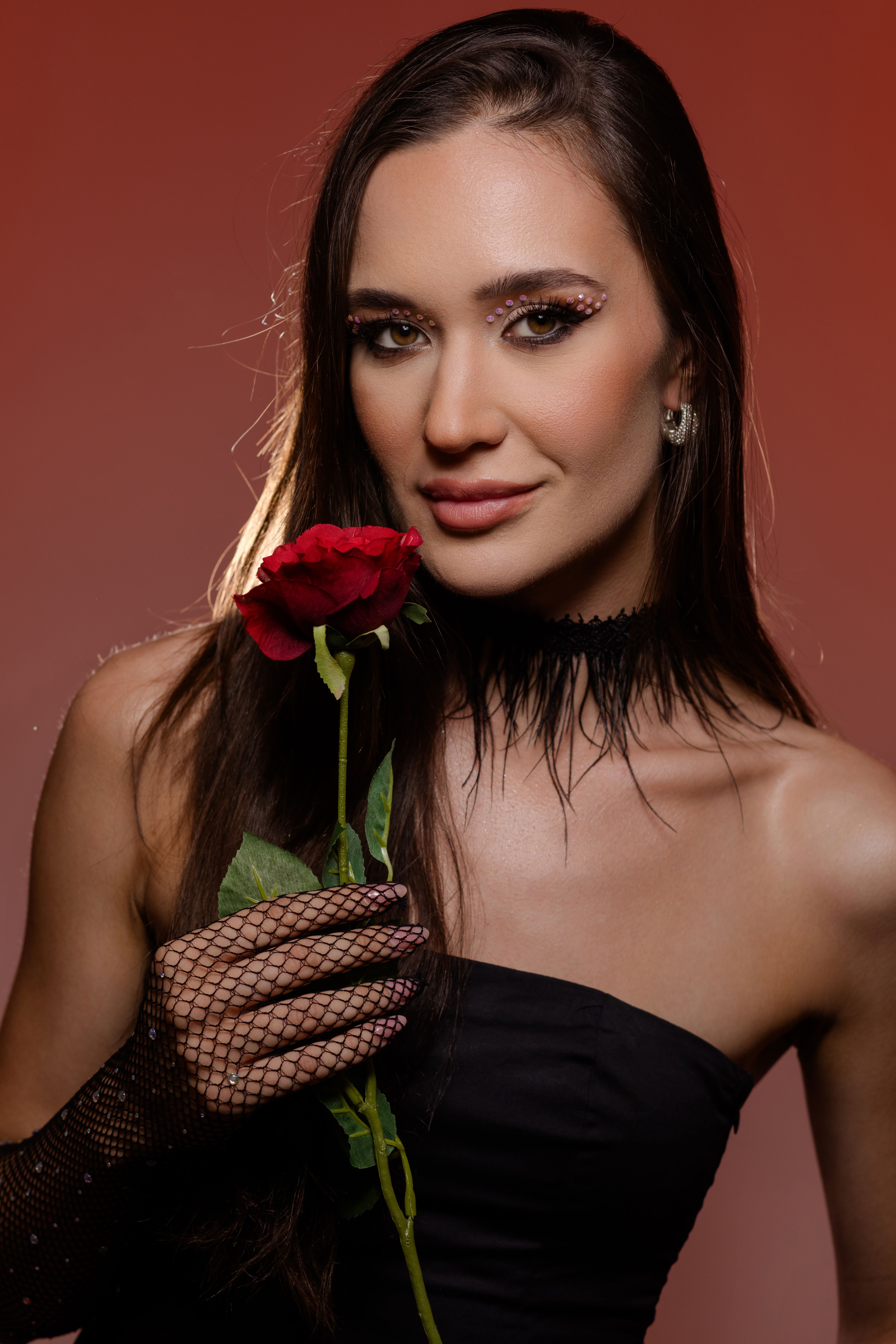 Elegant portrait of a woman holding a red rose with glamorous makeup and netted gloves.
