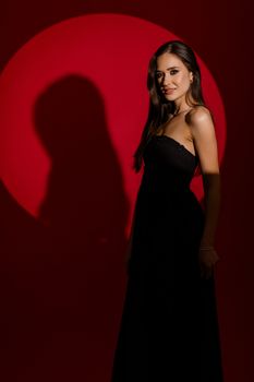 Woman in a sleek black dress stands elegantly with a red circular backdrop, creating a dramatic portrait.