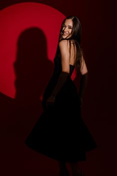 Stylish woman in a black dress poses elegantly against a red backdrop.