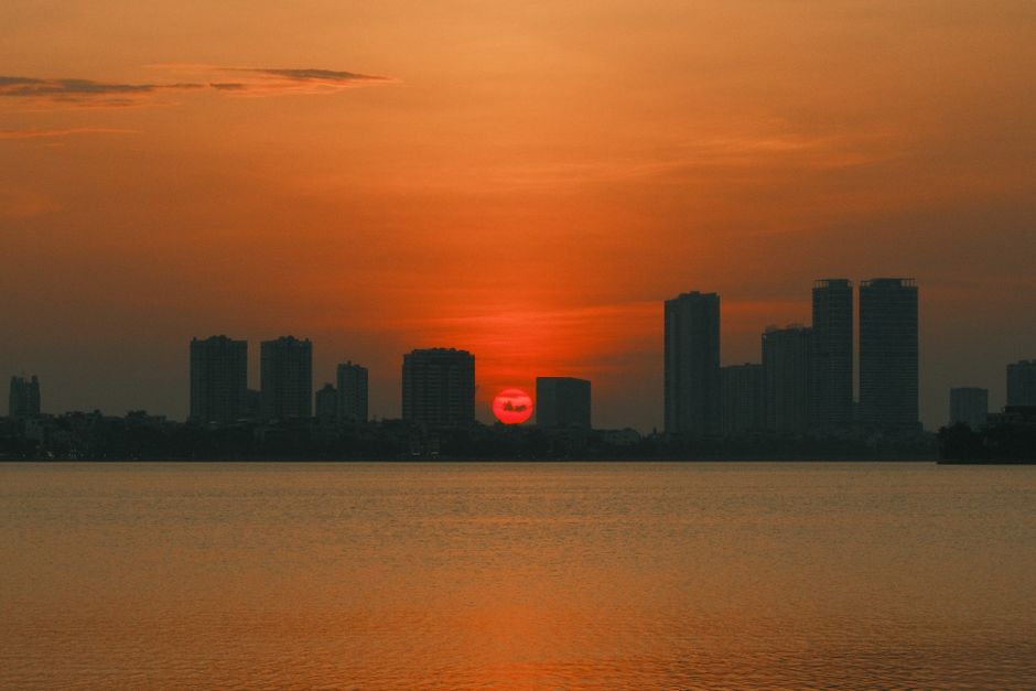 Breathtaking sunset over Hanoi's skyline reflecting on tranquil water with vivid orange hues.
