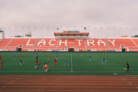 Players engaged in a soccer match at Lạch Tray Stadium, Hải Phòng, Vietnam. Cloudy day setting.