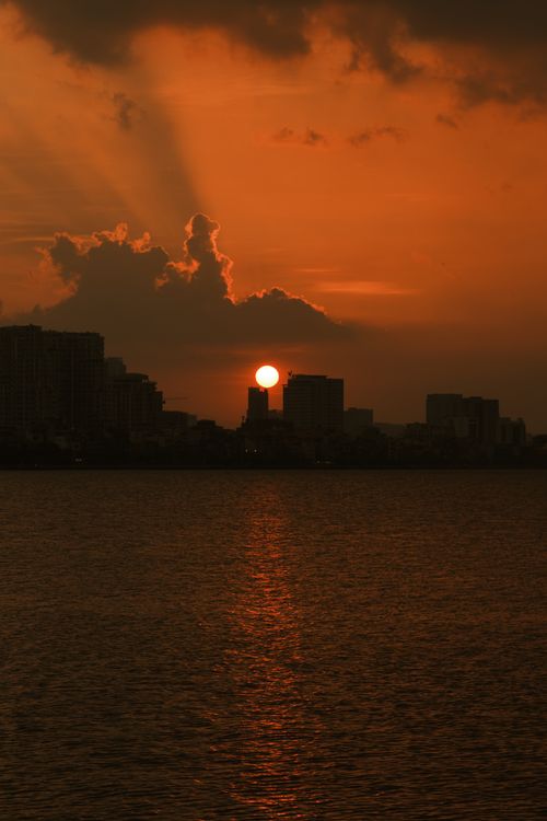 Free Beautiful sunset casting an orange glow over West Lake in Hanoi, Vietnam, with city skyline silhouettes. Stock Photo