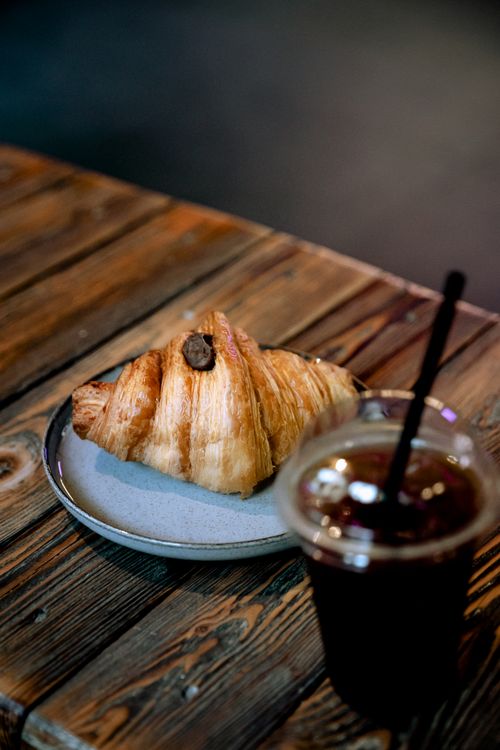 Free Tasty croissant paired with iced coffee on a rustic wooden table in a cozy cafe. Stock Photo