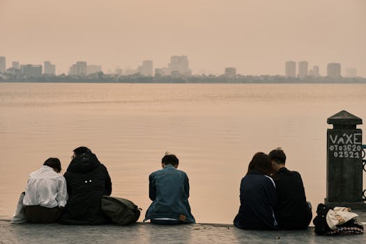 A group of young adults sitting by the tranquil West Lake in Hanoi, Vietnam during sunset.