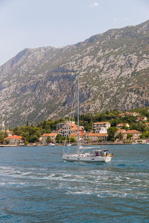 Free Idyllic sailboat scene on a bay with mountainous backdrop and coastal houses under a clear sky. Stock Photo