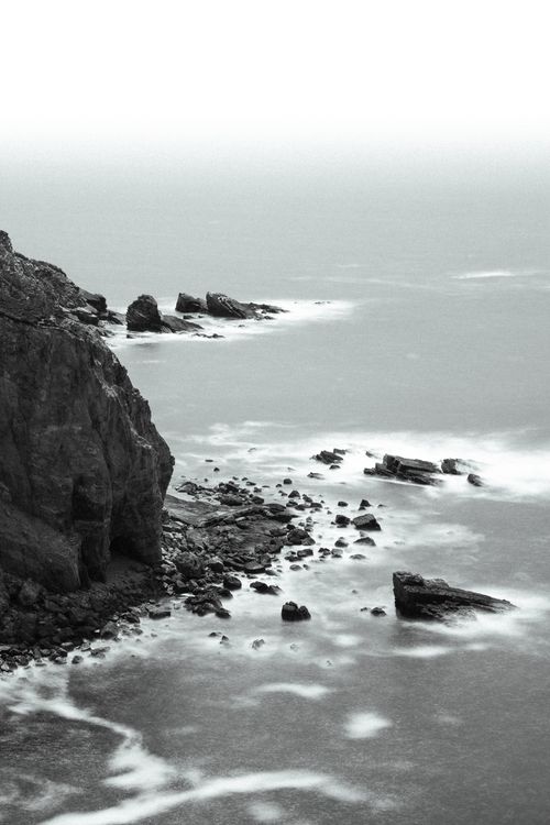 Free Tranquil black and white photo of a rugged coastal cliff and waves. Stock Photo