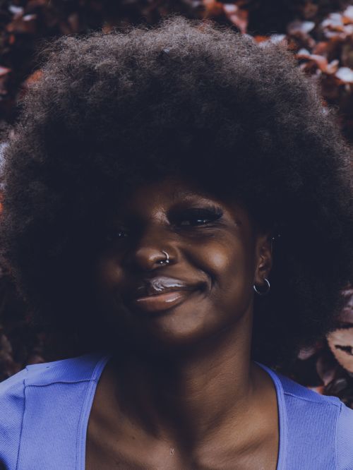 Free Smiling woman with afro hairstyle wearing blue, surrounded by autumn leaves. Stock Photo