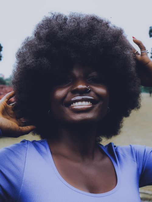 Free A joyful woman with an afro hairstyle smiling brightly outdoors in Abuja, Nigeria. Stock Photo