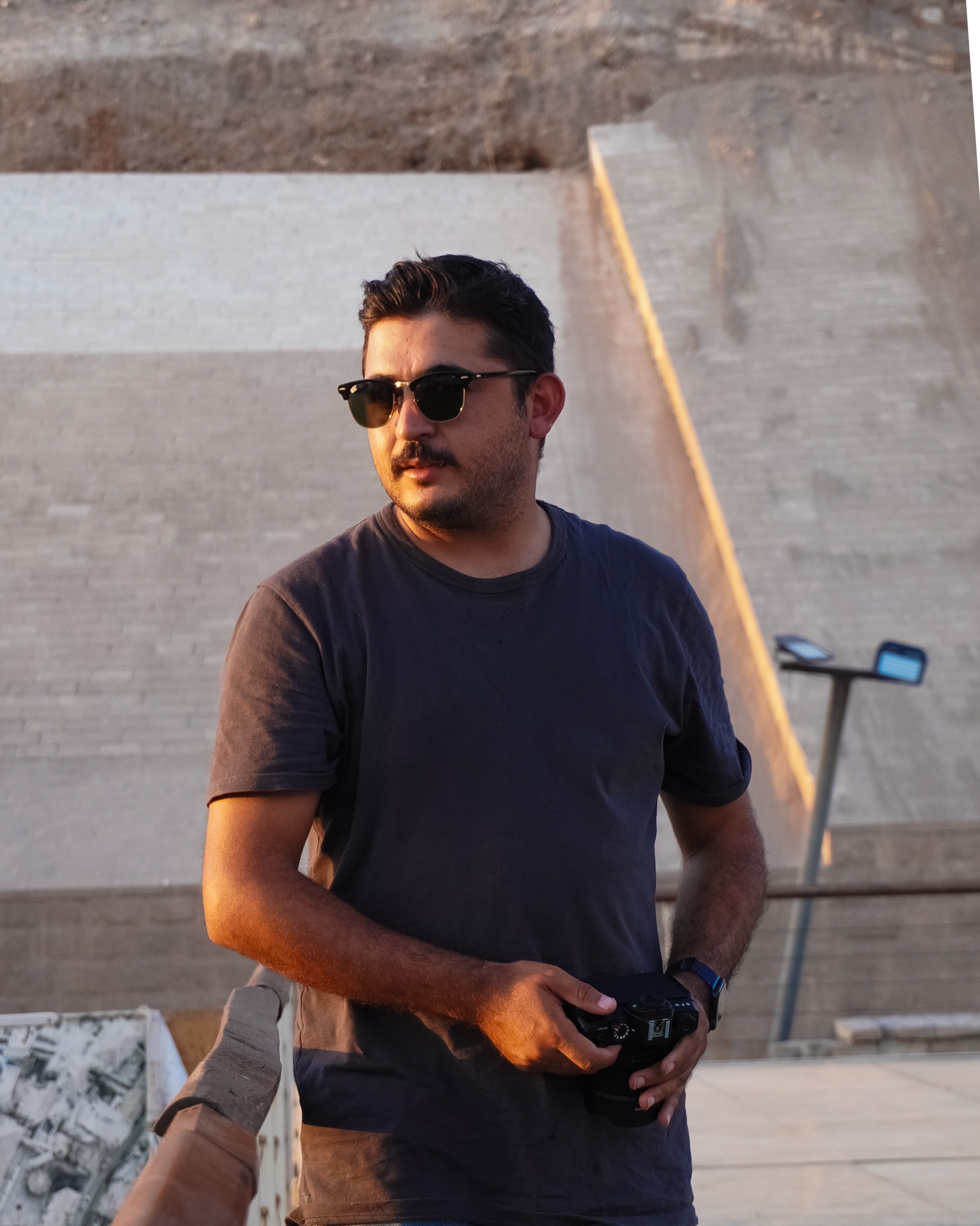 Stylish man wearing sunglasses outdoors in warm evening light.