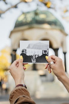 Person holding postcard of Istanbul in front of the German Fountain on a sunny day.