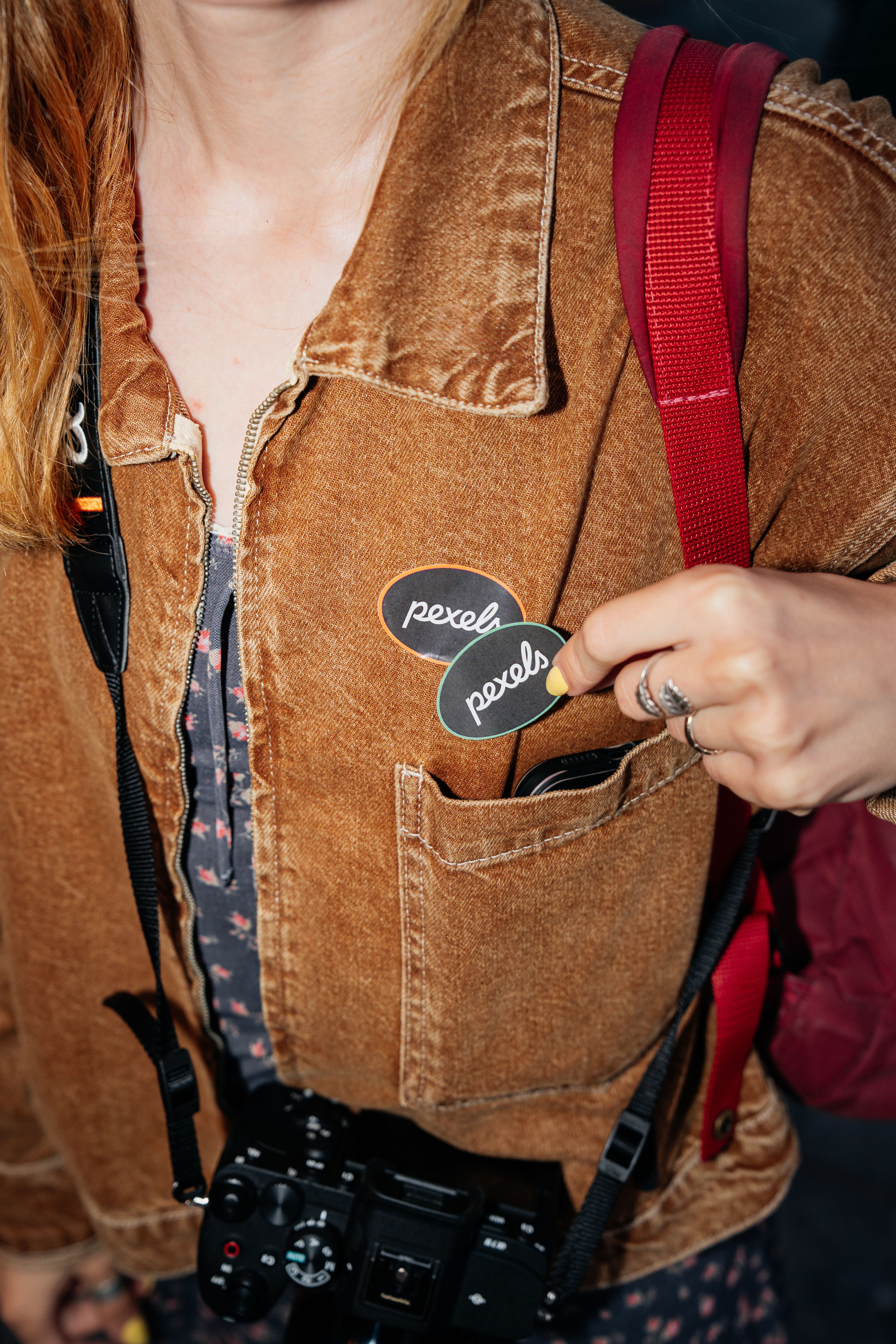 Person in brown jacket holding camera and badges in pocket.