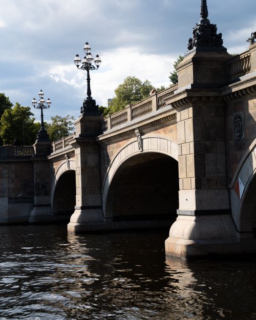 Free Elegant historical stone bridge with ornate details spanning a tranquil river under clear skies. Stock Photo