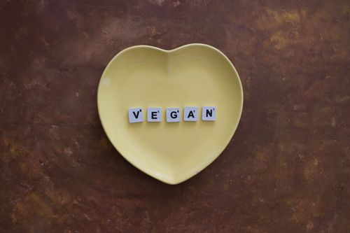 Free Yellow heart plate with letters spelling 'VEGAN' on a brown textured background. Stock Photo