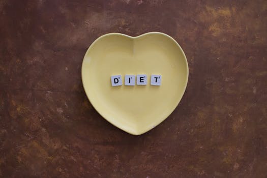 A heart-shaped yellow plate with scrabble tiles spelling 'Diet' on a brown textured background.