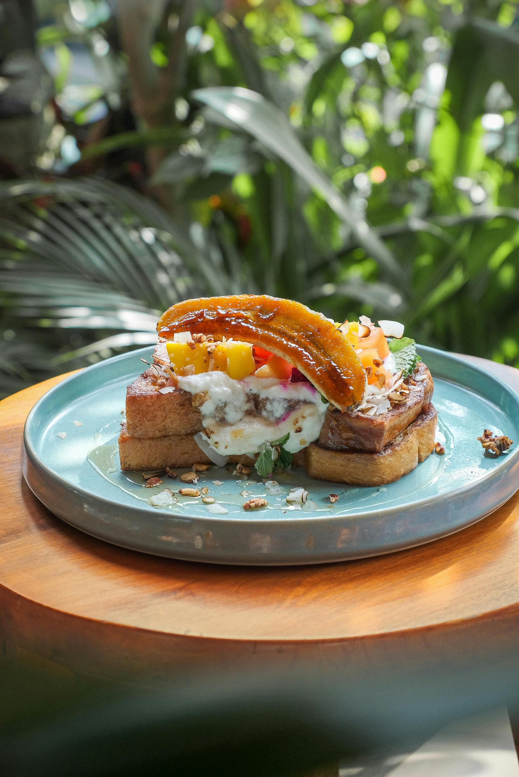 A vibrant plate of French toast topped with tropical fruits and cream, captured outdoors in Bali.