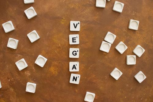 Free Flat lay of scattered scrabble tiles spelling 'VEGAN' on a rustic brown background. Stock Photo