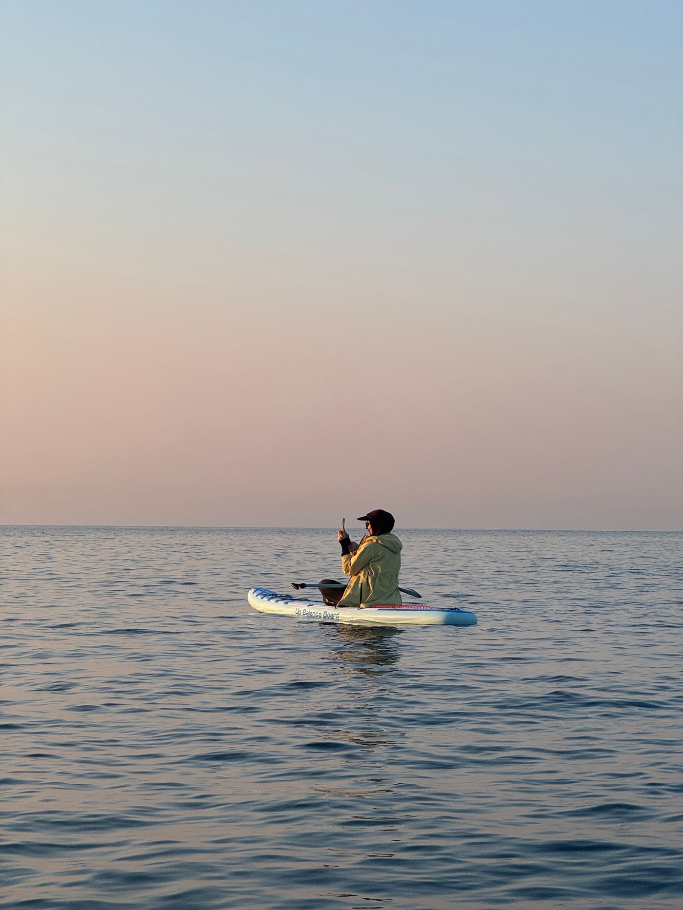 Solitary paddleboarder moving across calm water at sunrise