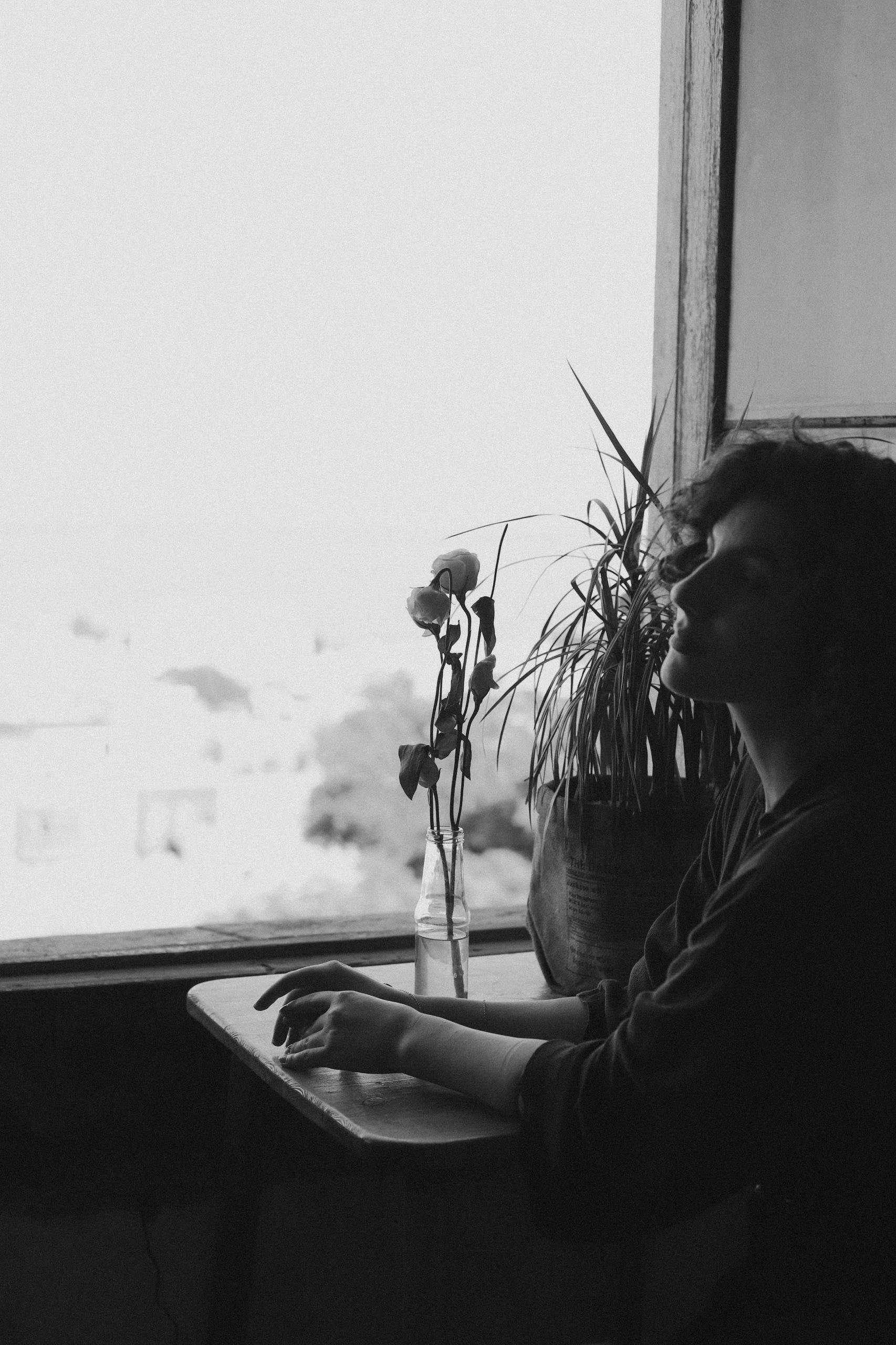 bezplatná Na černobílé fotografii sedí žena zamyšleně u okna a evokuje klidné zamyšlení. Základová fotografie