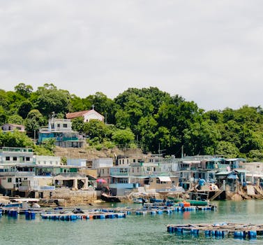 Idyllic fishing village with colorful houses by lush green hillside and calm waters.