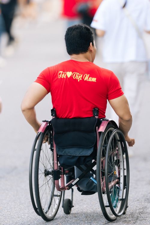 Free Man in a red shirt, promoting Vietnam, in a wheelchair on a busy street. Stock Photo
