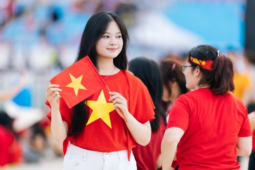 Free A young woman in a red t-shirt holds the Vietnam national flag, showcasing national pride at an outdoor event. Stock Photo