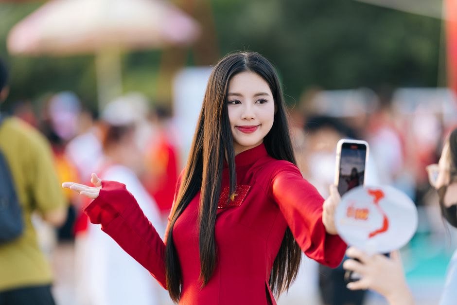 A young woman in a vibrant red outfit poses for a selfie outdoors, capturing a joyful moment.