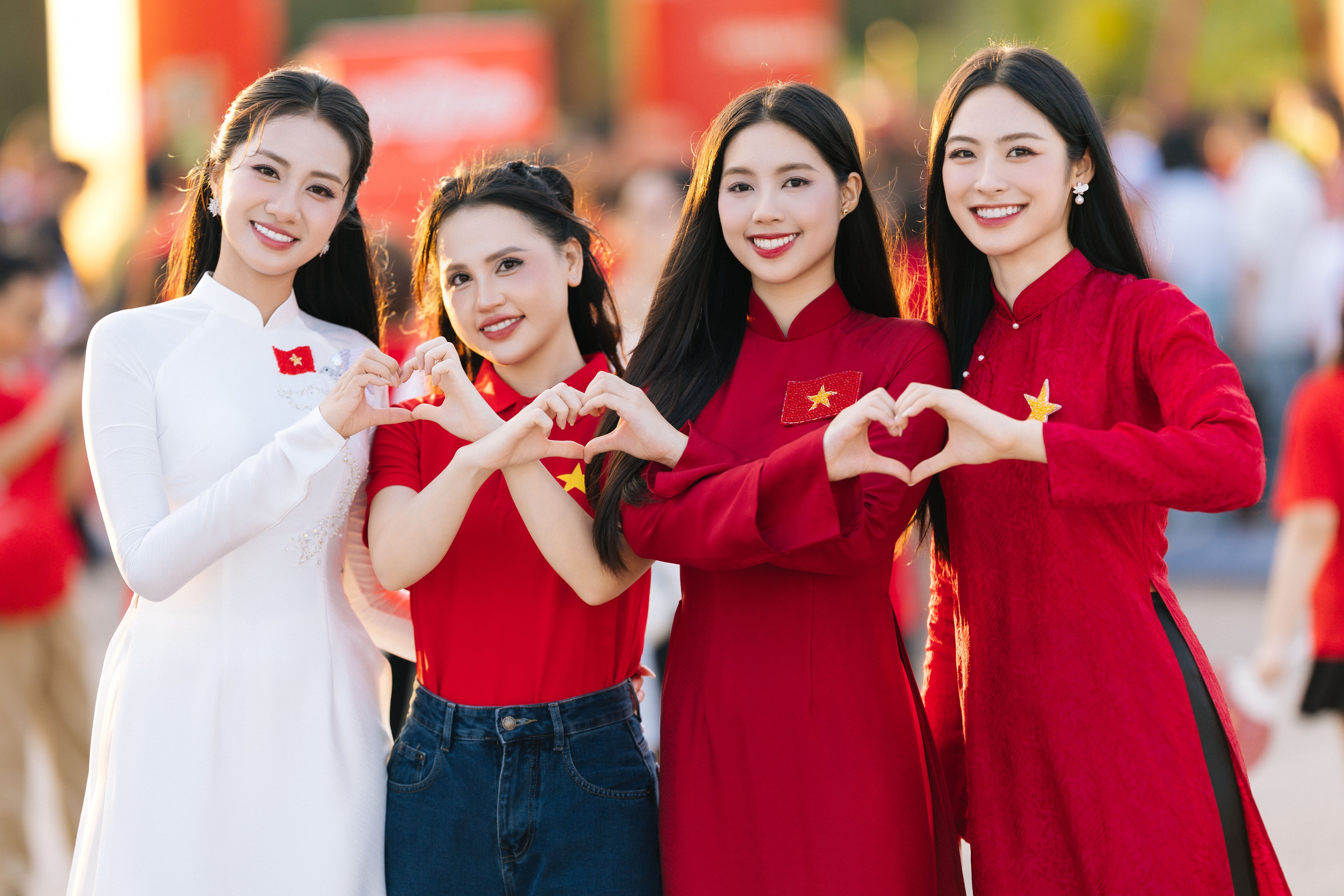 Four Vietnamese women in red and white outfits making heart shapes. Bright and vibrant atmosphere.