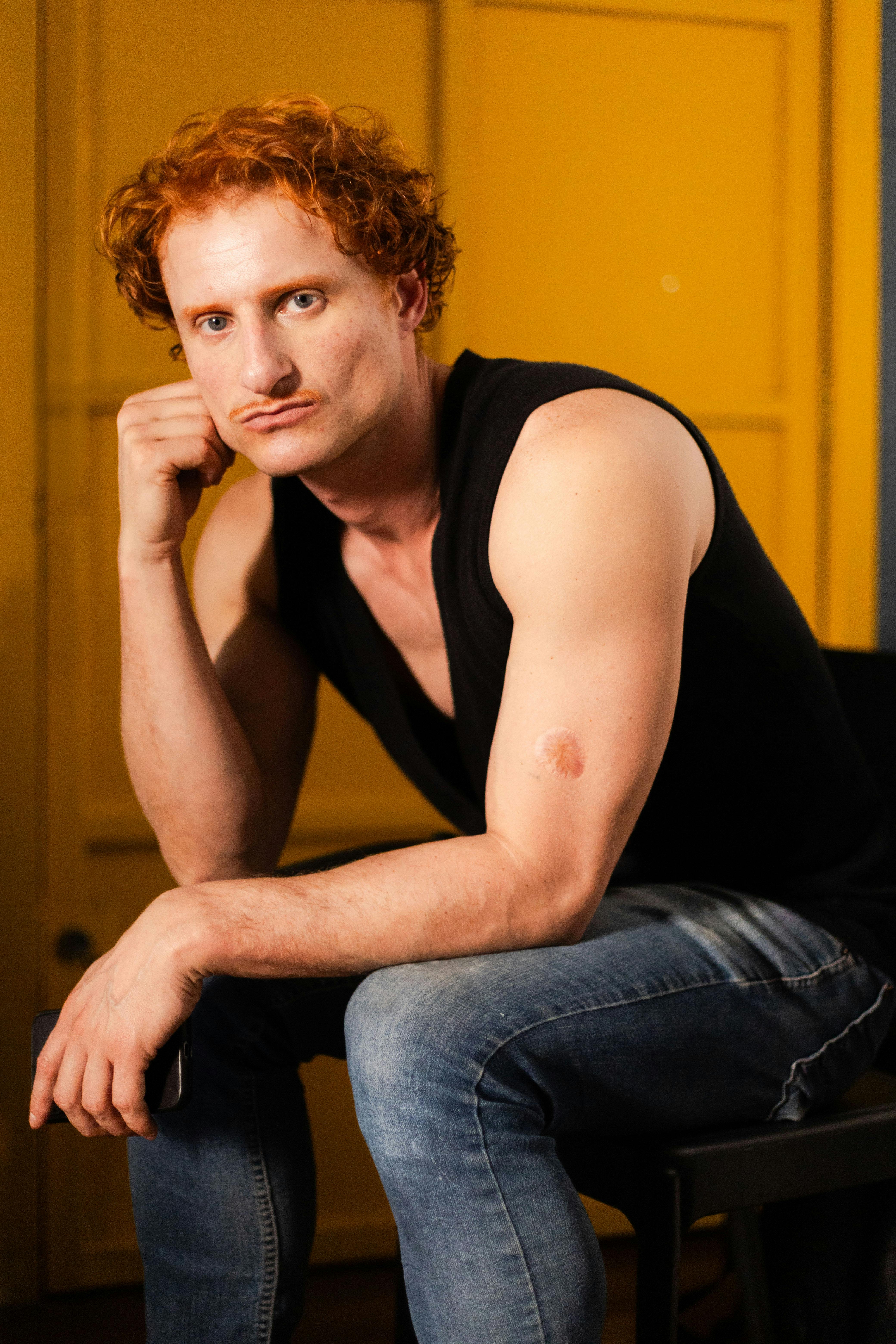 Artistic studio portrait featuring a man with red hair seated against a yellow background.