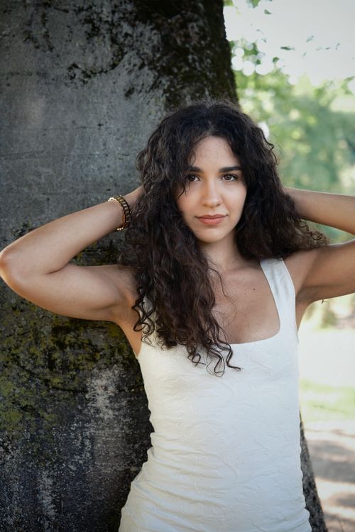 Free Natural light portrait of a woman with curly hair leaning against a tree outdoors. Stock Photo