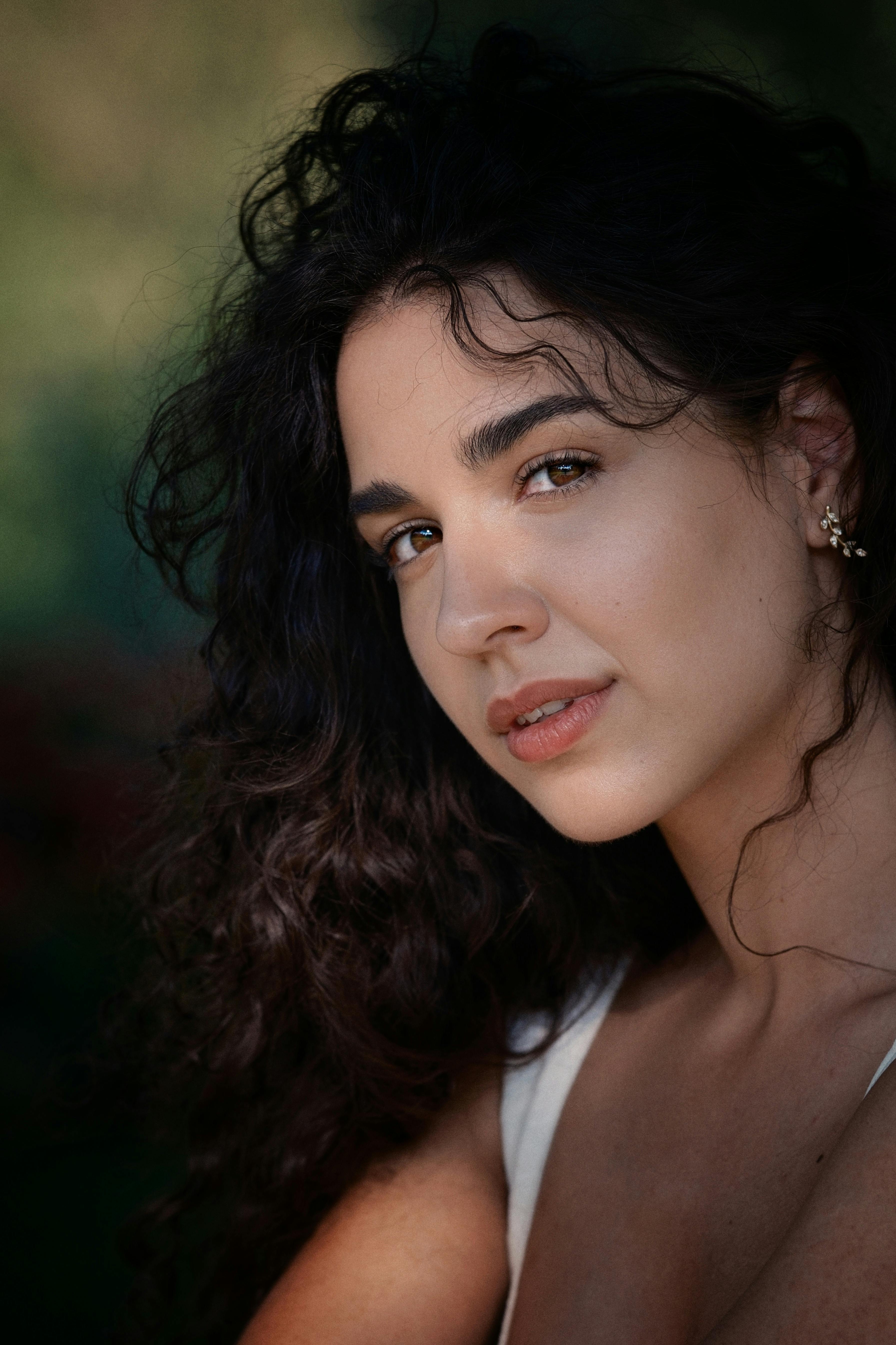 Close-up portrait of a woman with curly hair and elegant earrings in natural light.