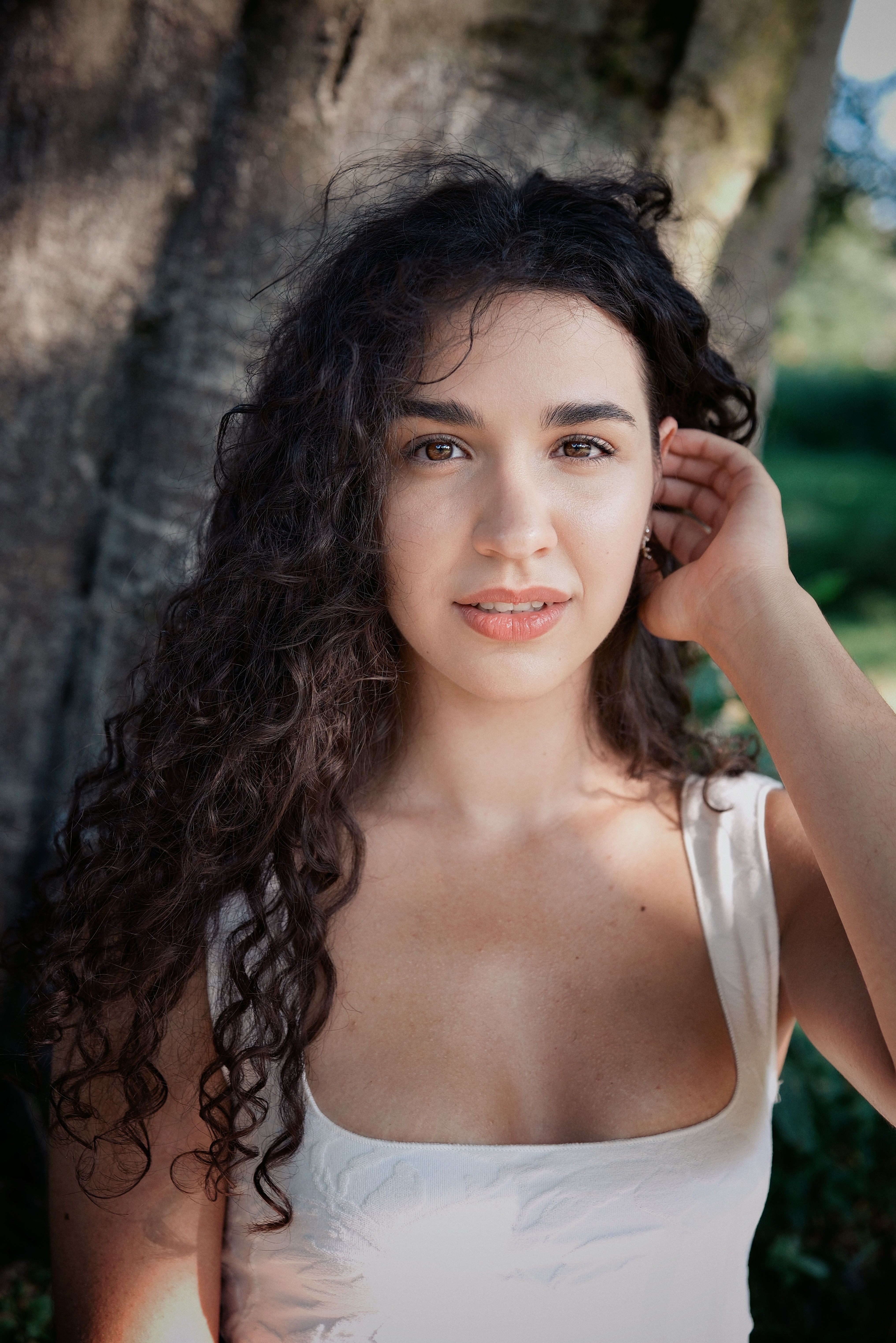 Natural outdoor portrait of a young woman with curly hair. Soft lighting and fresh scenery enhance her serene expression.