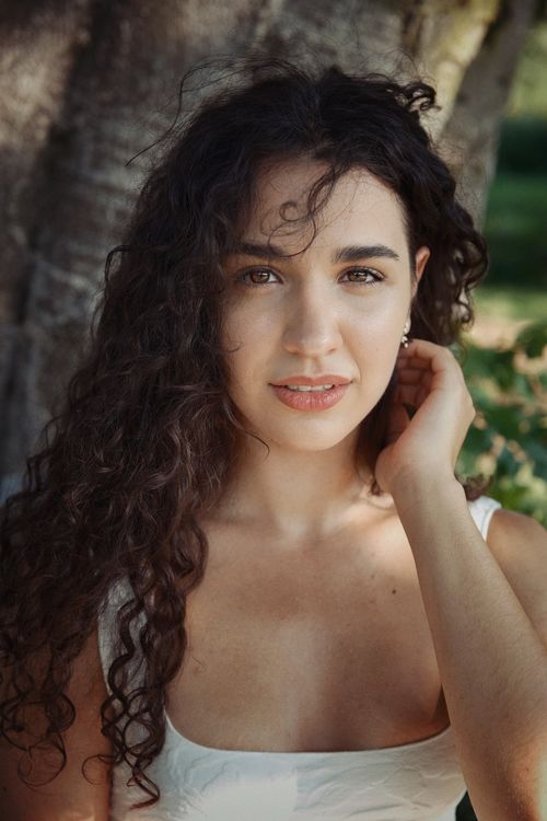 Free Young woman with curly hair poses outdoors in natural sunlight. Stock Photo