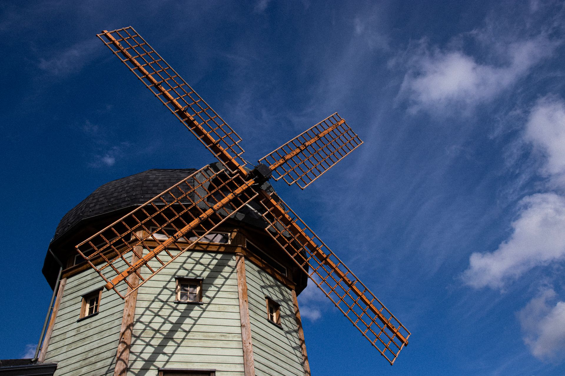 Vintage windmill with wooden blades under a vibrant blue sky.